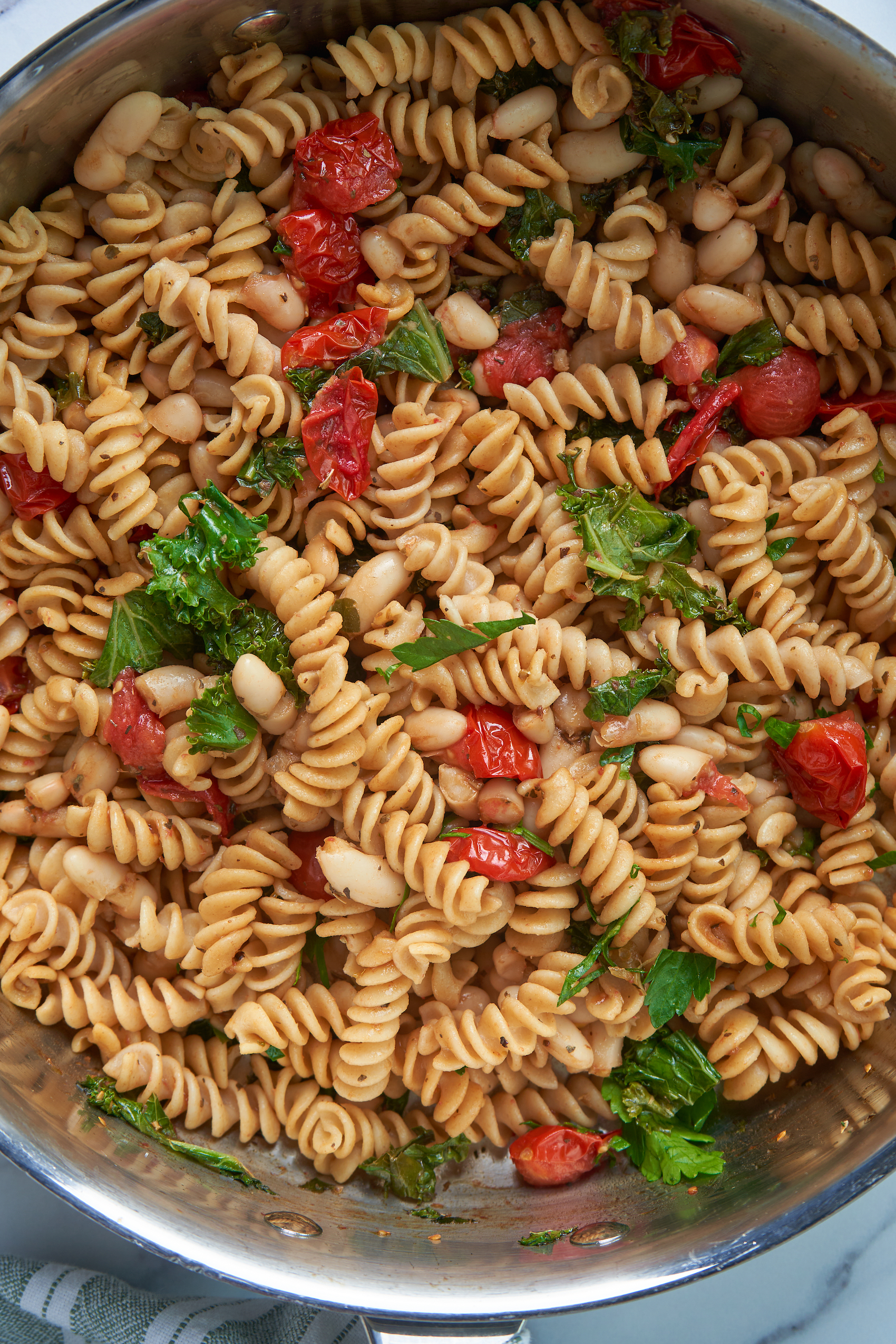 a closeup of a pot of pasta cooked with tomatoes, white beans and chopped kale