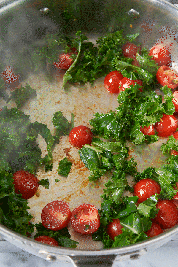 halved cherry tomatoes and shredded kale being sauteed in a skillet