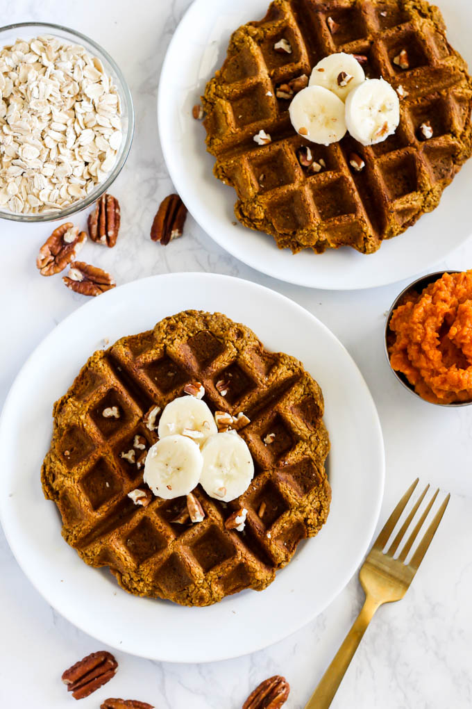 two plates, each with a pumpkin waffle topped with sliced bananas