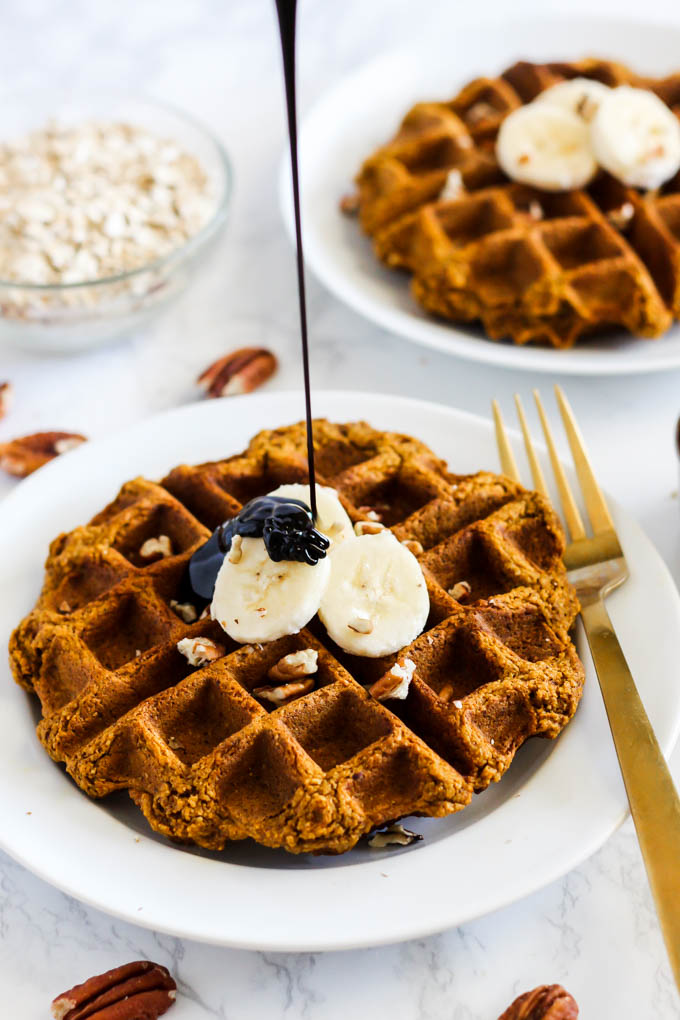 a waffle topped with sliced bananas and pecans being drizzled with molasses