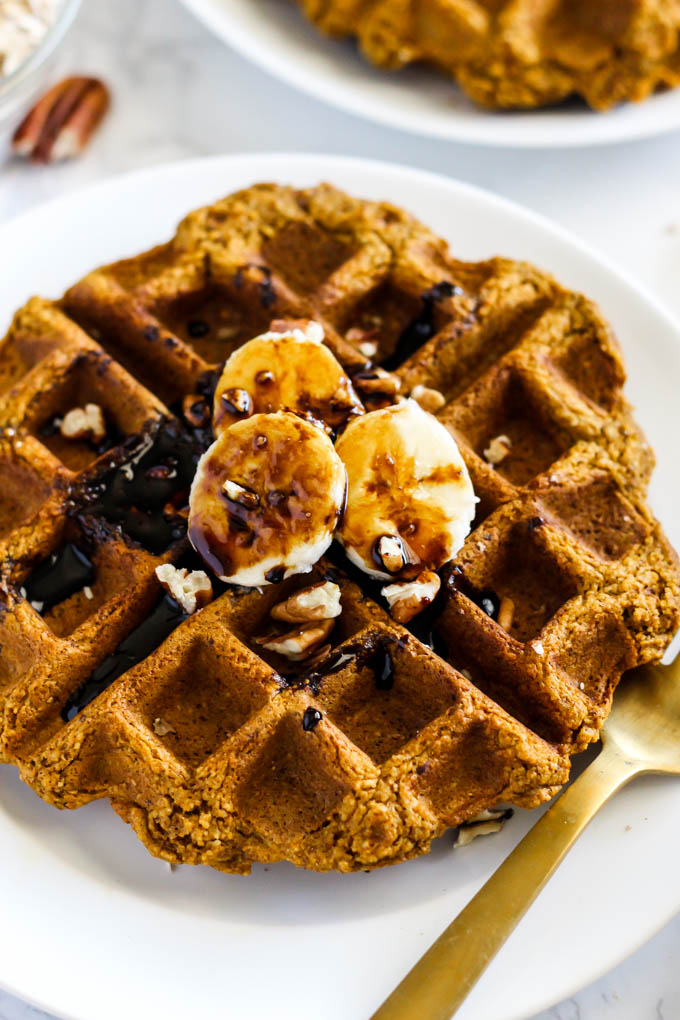 a plate with a pumpkin waffled topped with bananas, pecans and molasses