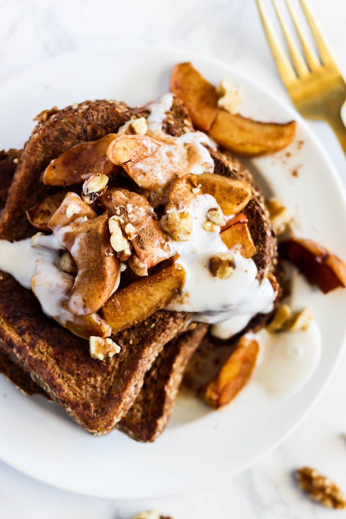 a plate of french toast topped with apples, walnuts and vegan yogurt
