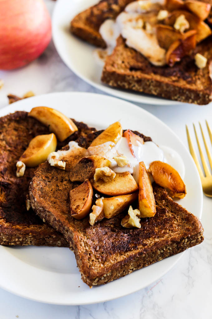 two plates of french toast topped with cinnamon, apples, nuts and vegan yogurt