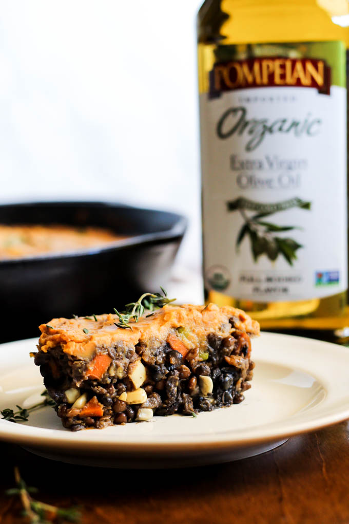 a slice of vegetarian shepherd's pie topped with thyme served next to a bottle of olive oil