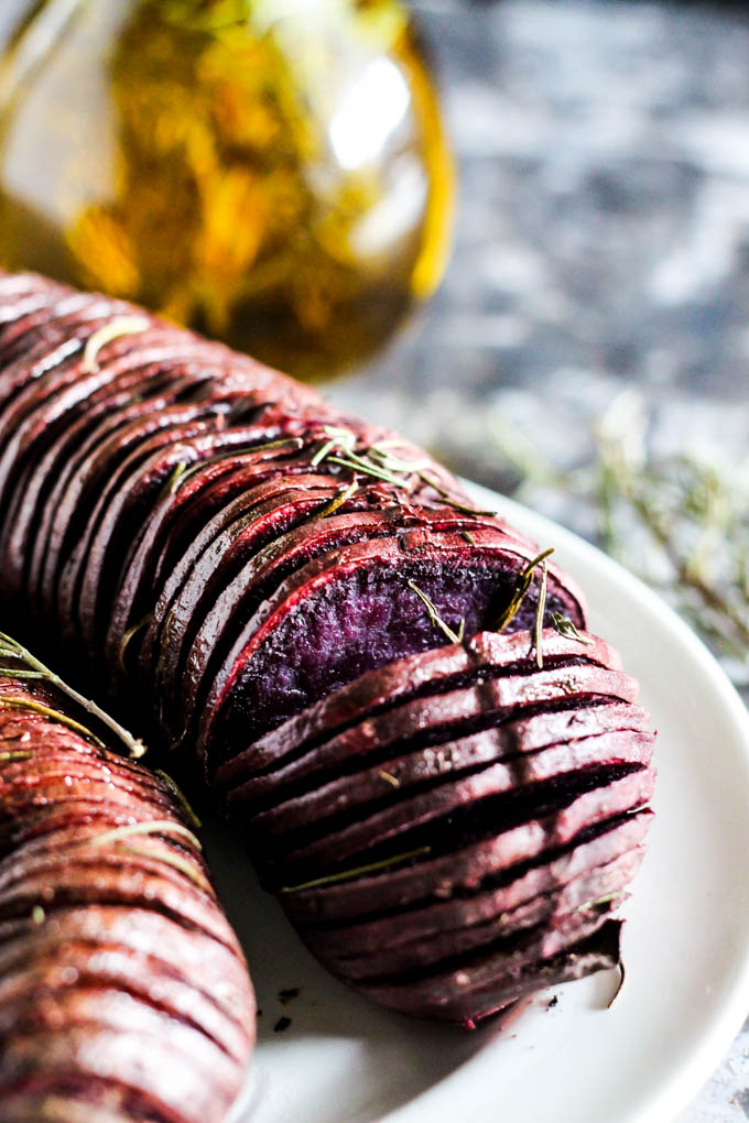 a hasselback purple sweet potato topped with rosemary
