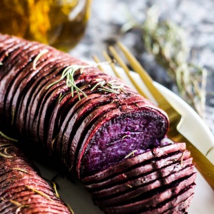 a hasselback style purple potato topped with rosemary