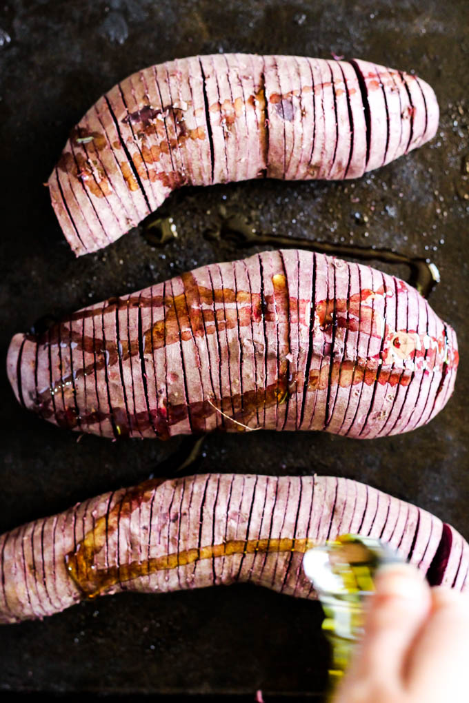 a bottle drizzling infused olive oil onto hasselback potatoes