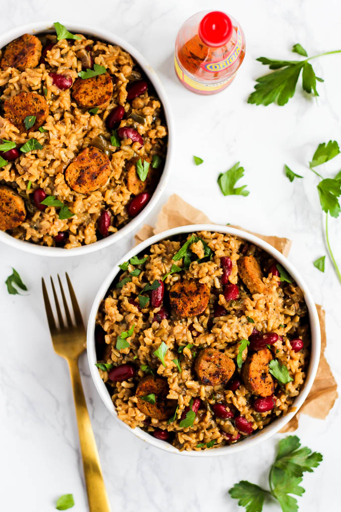 two bowls of vegetarian jambalaya next to a bottle of hot sauce