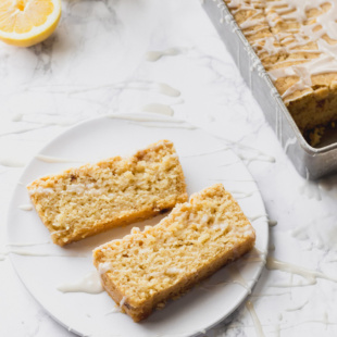 two slices of lemon cake served on a white dish next to a tin holding the full loaf