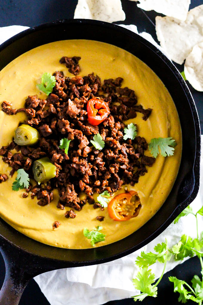 a skillet of vegan queso topped with chipotle chili, cilantro and sliced peppers