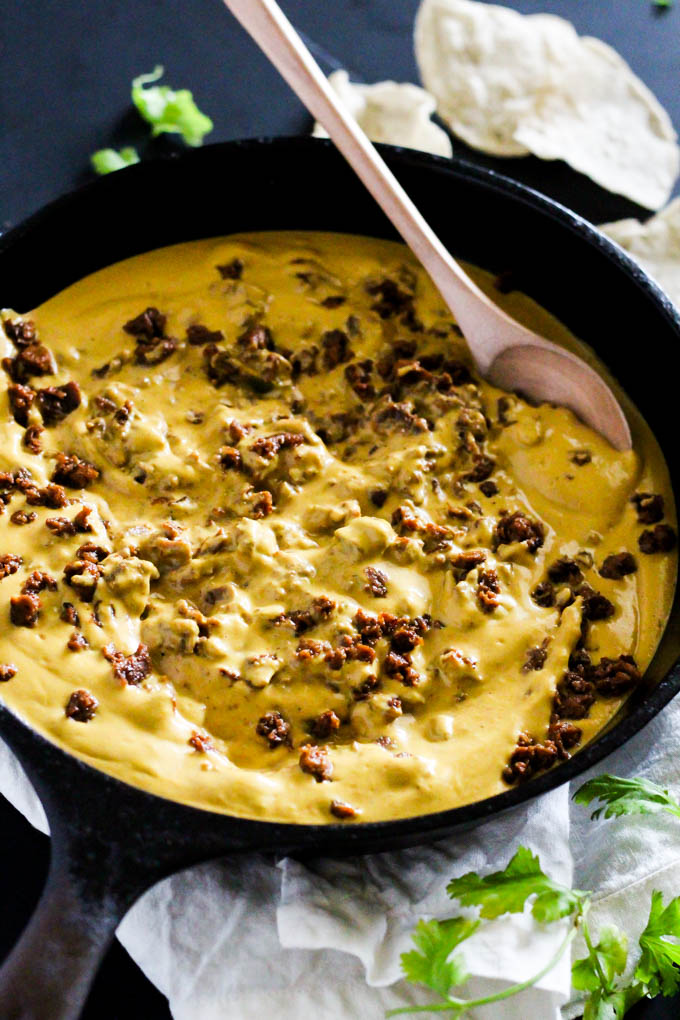 a wooden spoon stirring a skillet of vegan chili cheese dip