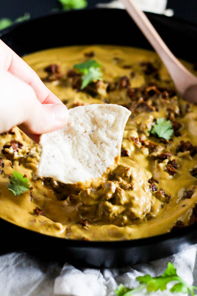 a tortilla chip scooping into a skillet of vegan chili cheese dip