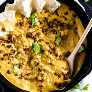 a cast iron skillet filled with vegan chili cheese dip being stirred with a wooden spoon