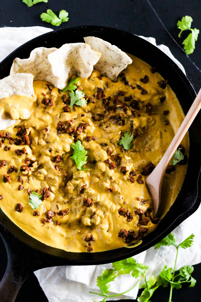 a cast iron skillet filled with vegan chili cheese dip being stirred with a wooden spoon