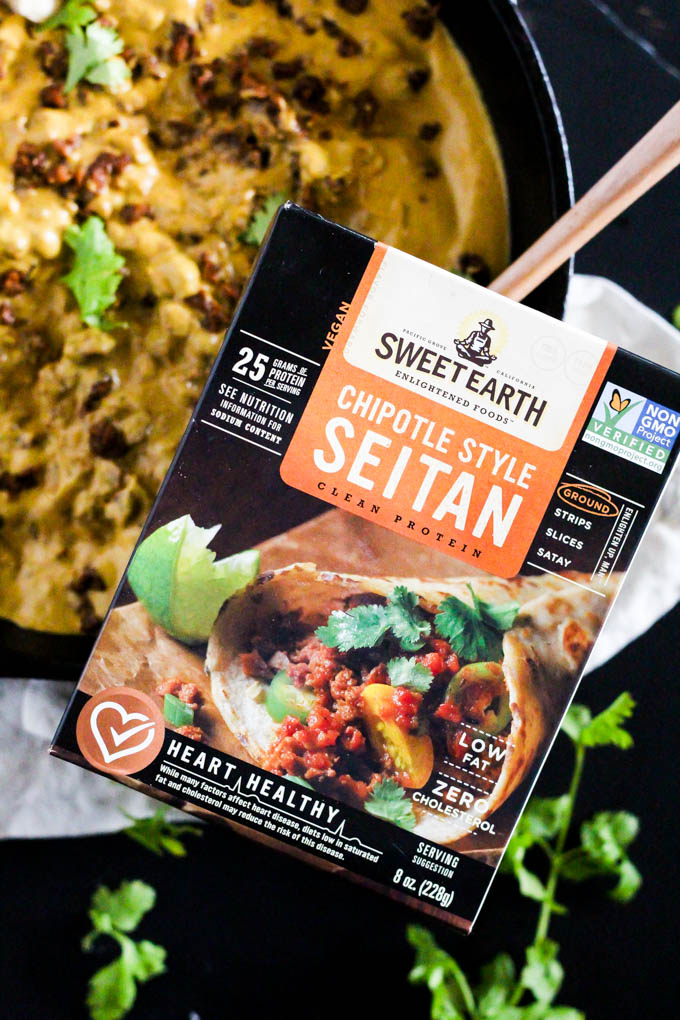 a box of chipotle style seitan held over a skillet of queso