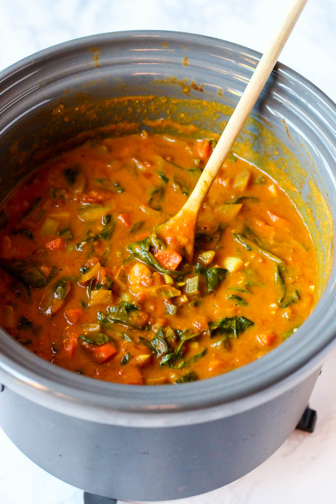 a vegan chickpea peanut stew being stirred in a slow cooker