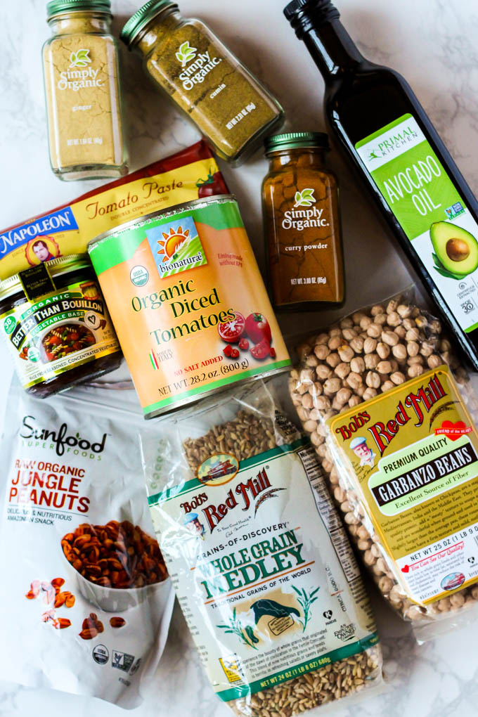 a bag of peanuts, a bag of grain medley, a bag of dried garbanzo beans, a bottle of avocado oil, a can of diced tomatoes, a jar of veggie bouillon, and bottles of cumin, ginger and curry powder