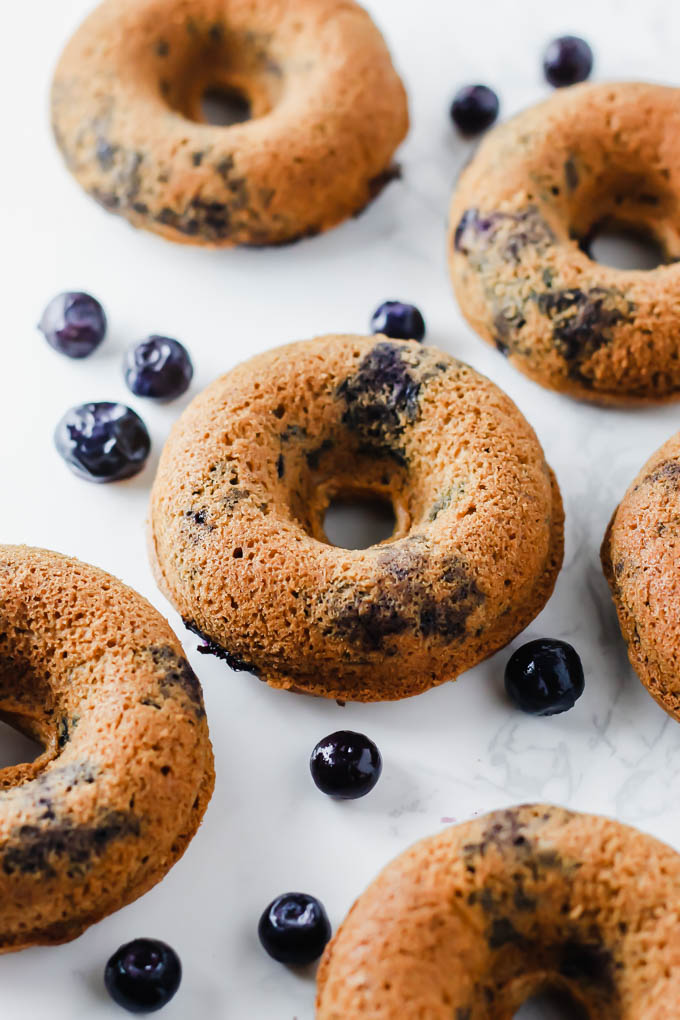 A close up shot of vegan gluten free blueberry donuts surrounded by scattered fresh blueberries