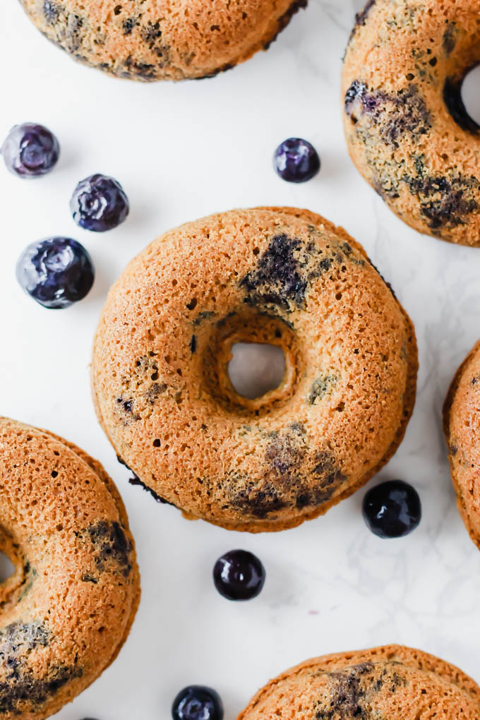 An overhead shot of a vegan blueberry doughnut surrounded by fresh blueberries