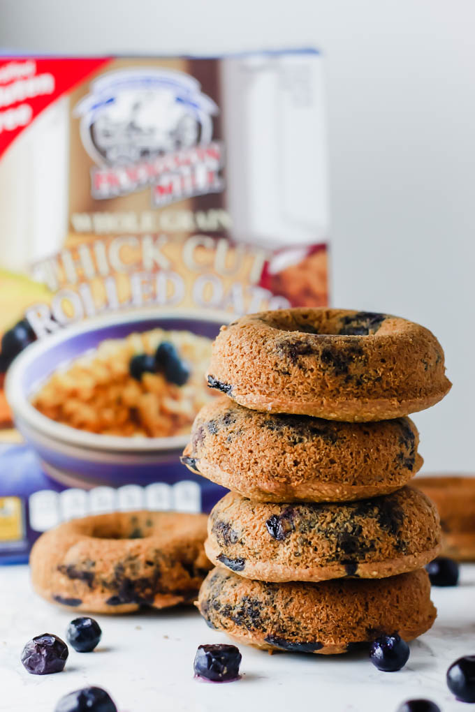 A stack of four blueberry vegan donuts in front of a box of gluten free oats