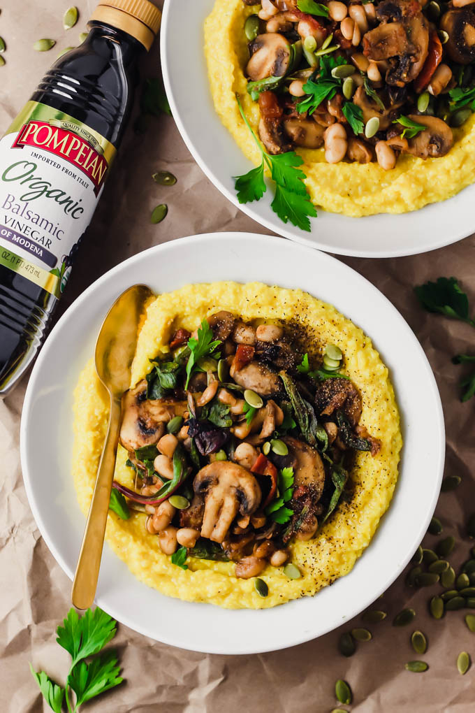 two bowls of vegan polenta with veggies next to a bottle of balsamic vinegar