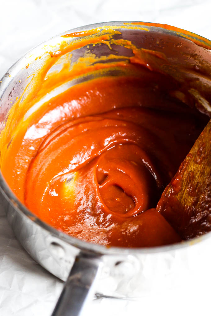 A pot of homemade vegan sweet and sour sauce being stirred with a wooden spoon