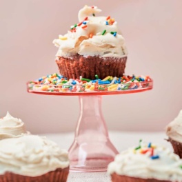 a red velvet cupcake topped with vanilla icing and rainbow sprinkles