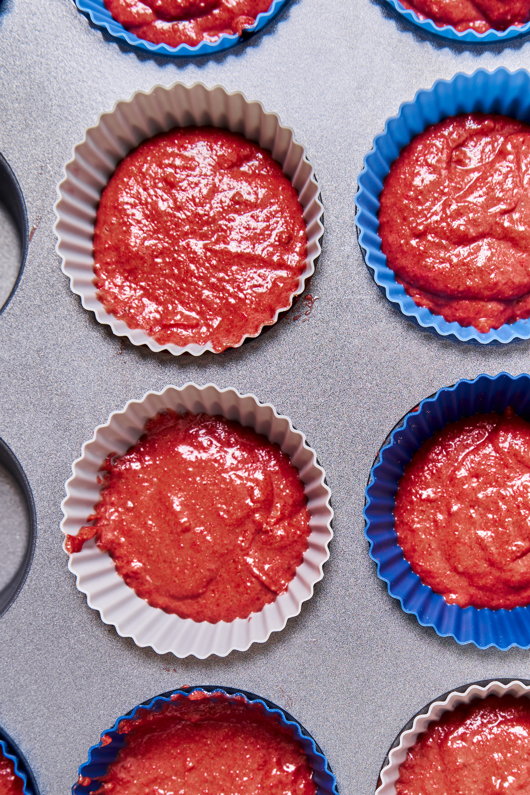 a cupcake tin with paper liners filled with red velvet cupcake batter