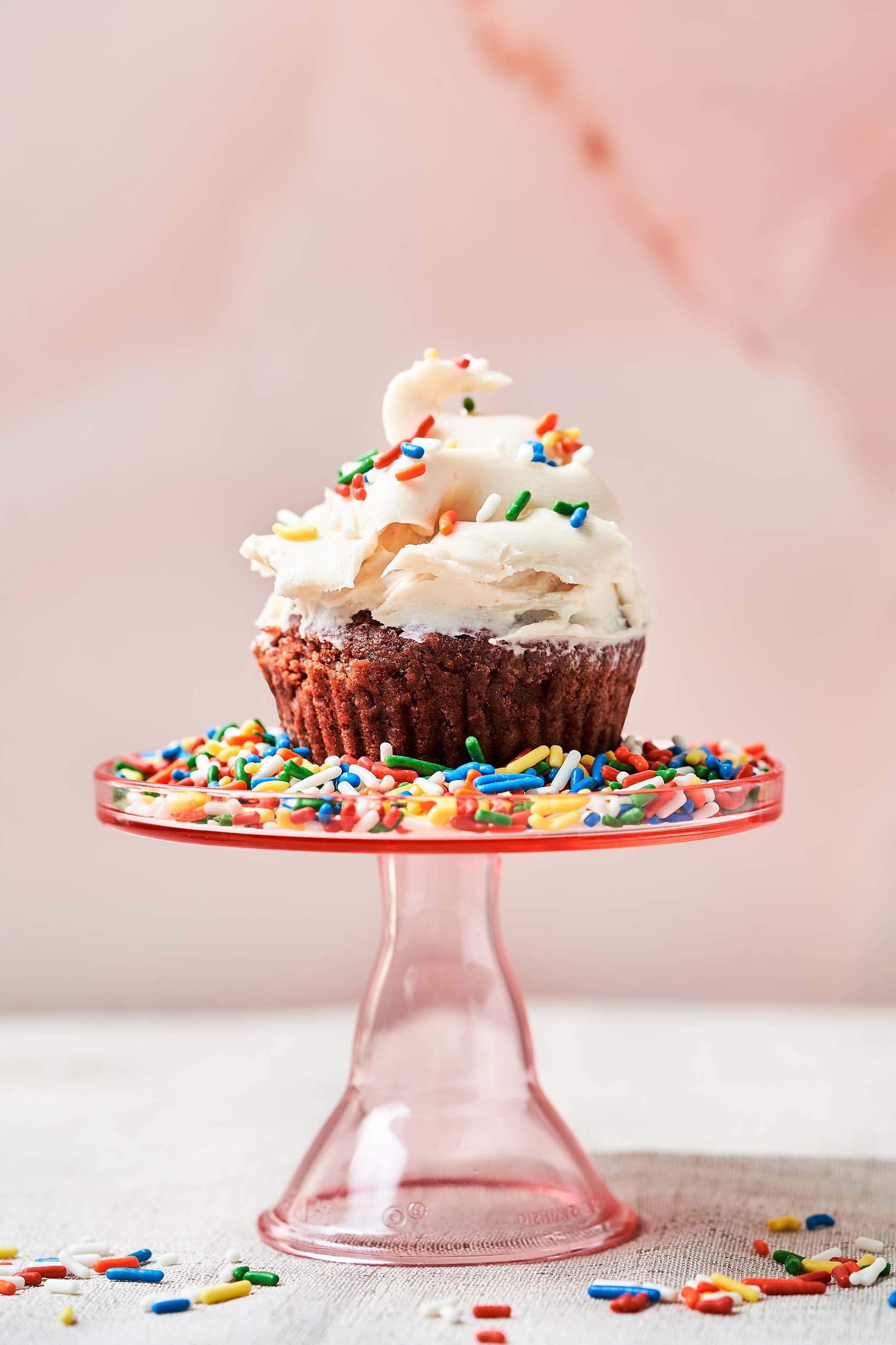 a red velvet cupcake topped with sprinkles sitting on a cake stand