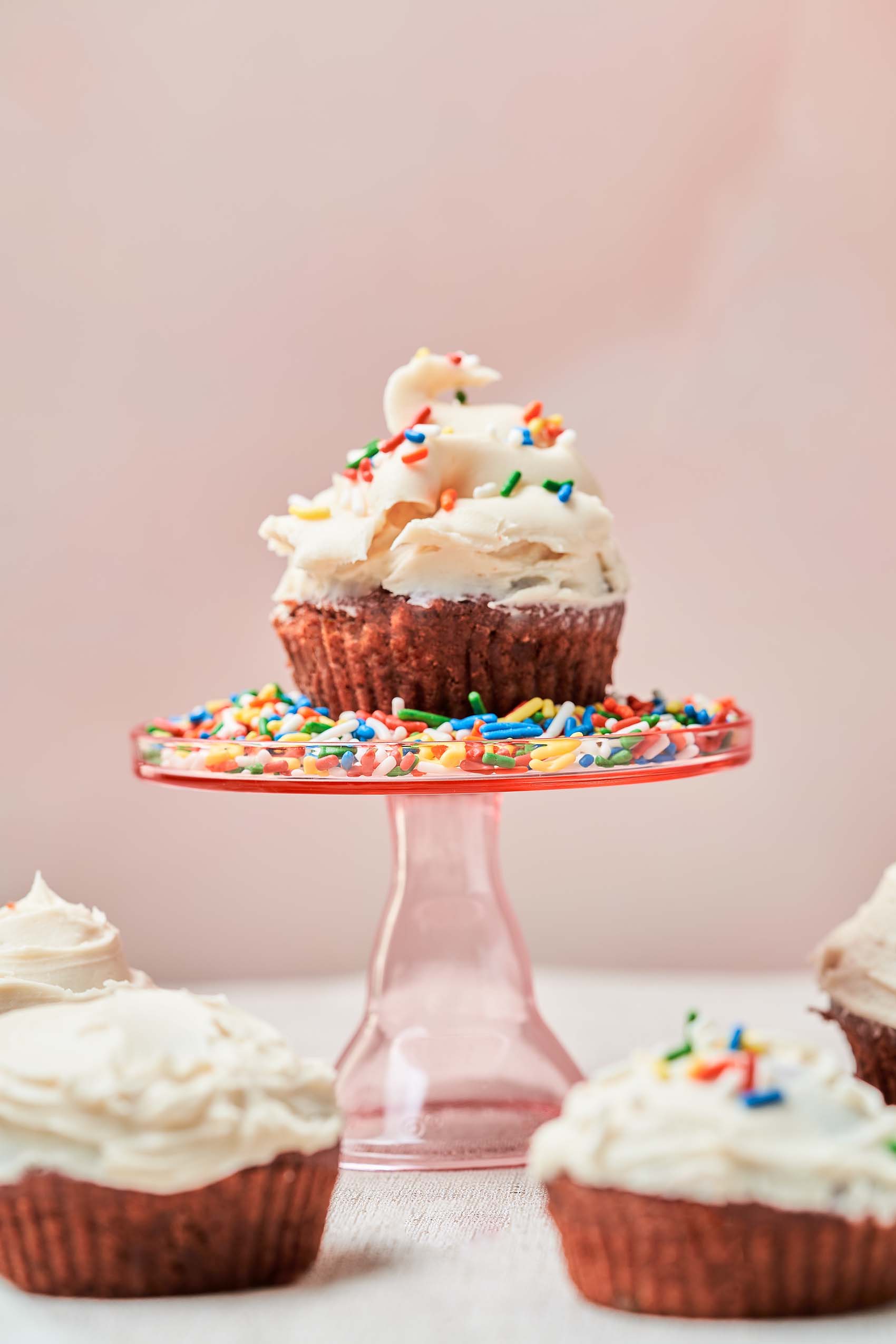 a red velvet cupcake topped with sprinkles and vanilla frosting