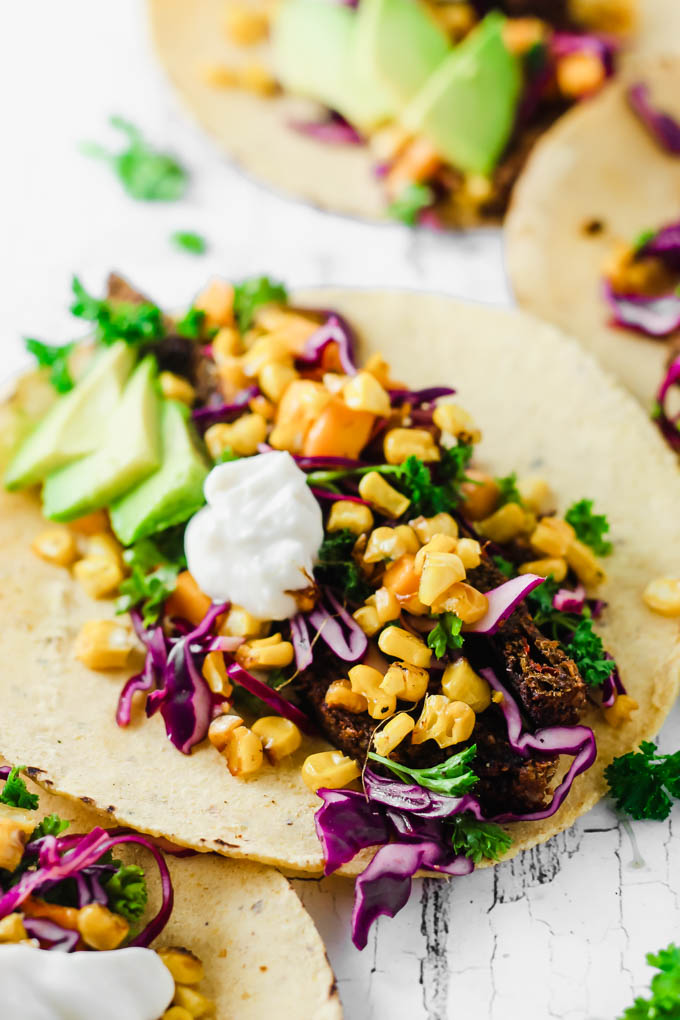 A vegan roasted corn taco filled with a veggie burger, mango slaw, vegan sour cream, and sliced avocado