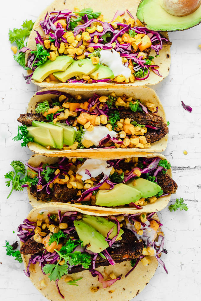 An overhead shot of four roasted corn tacos, all topped with sliced avocado and cilantro, served along side a half an avocado