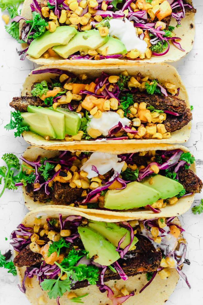 A close up of four vegan roasted corn tacos topped with mango slaw, avocado, and cilantro