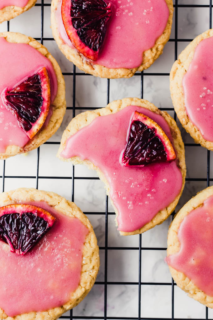 A vegan sugar cookie with a bite missing rests on a cooling rack surrounded by other sugar cookies