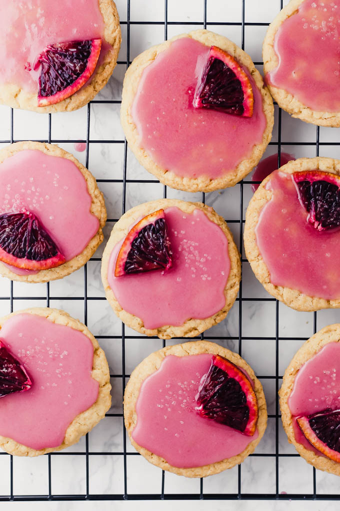 nine vegan sugar cookies topped with blood orange glaze sit on a cooling rack