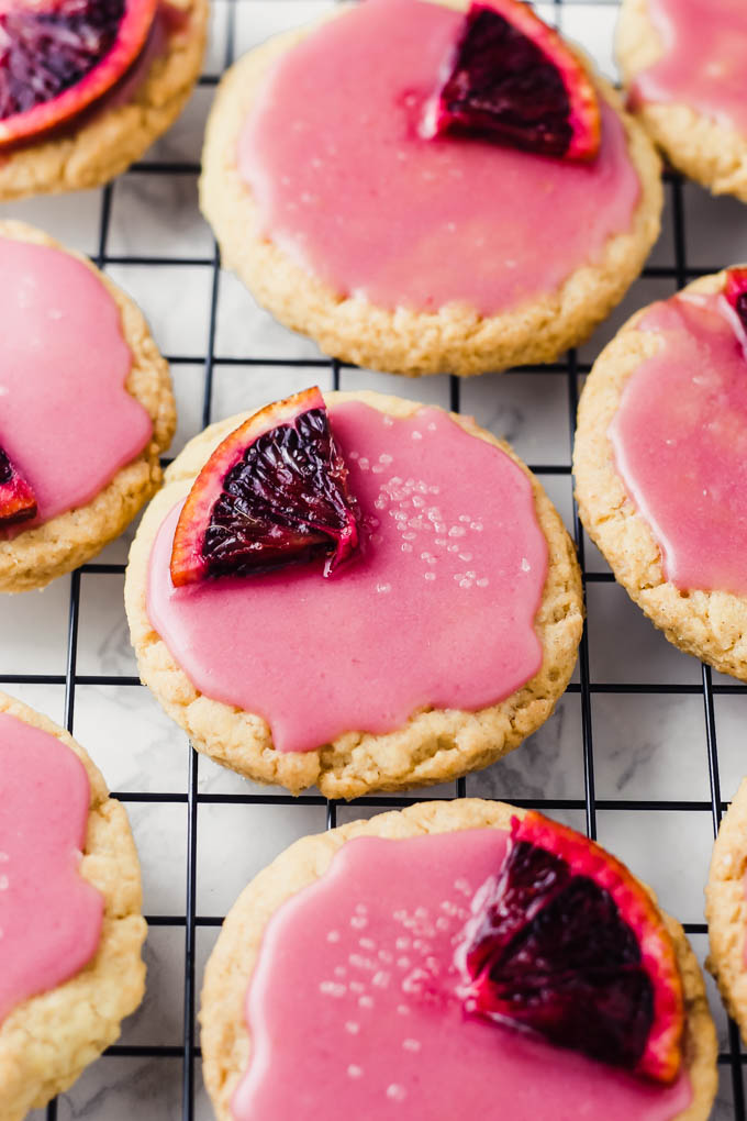 Sugar cookies with blood orange glaze rest on a cooling rack