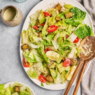 a plate of caesar salad next to a jar of homemade dressing