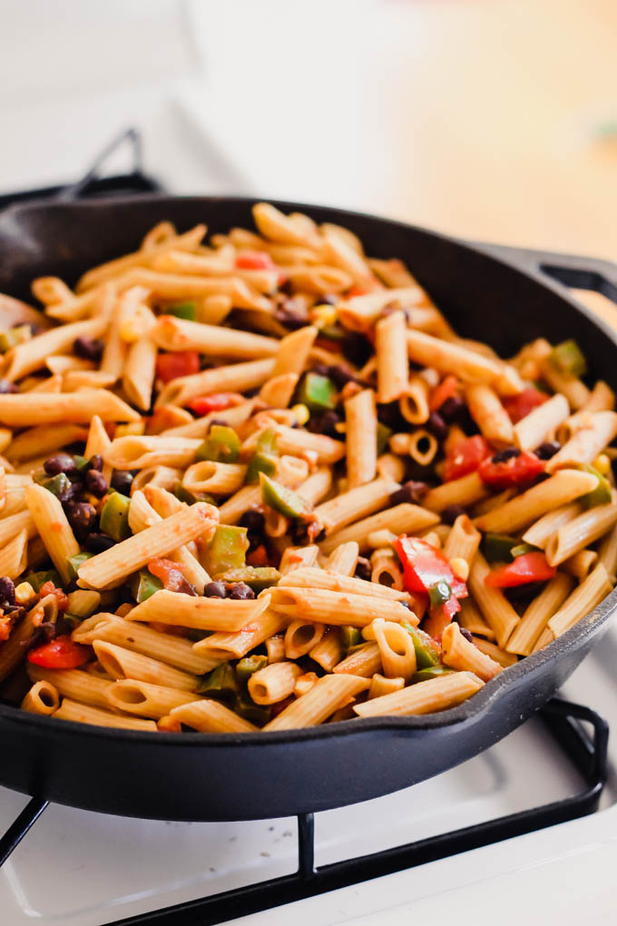a skillet of pasta on the stove with black beans and chopped bell peppers