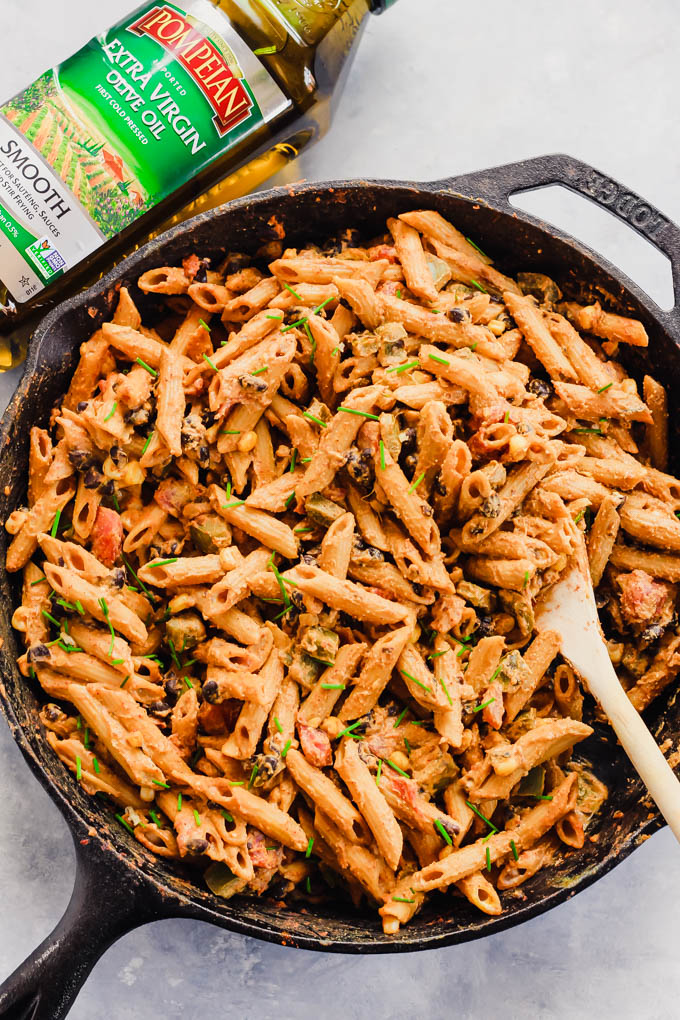 a cast iron skillet of Mexican pasta next to a bottle of olive oil