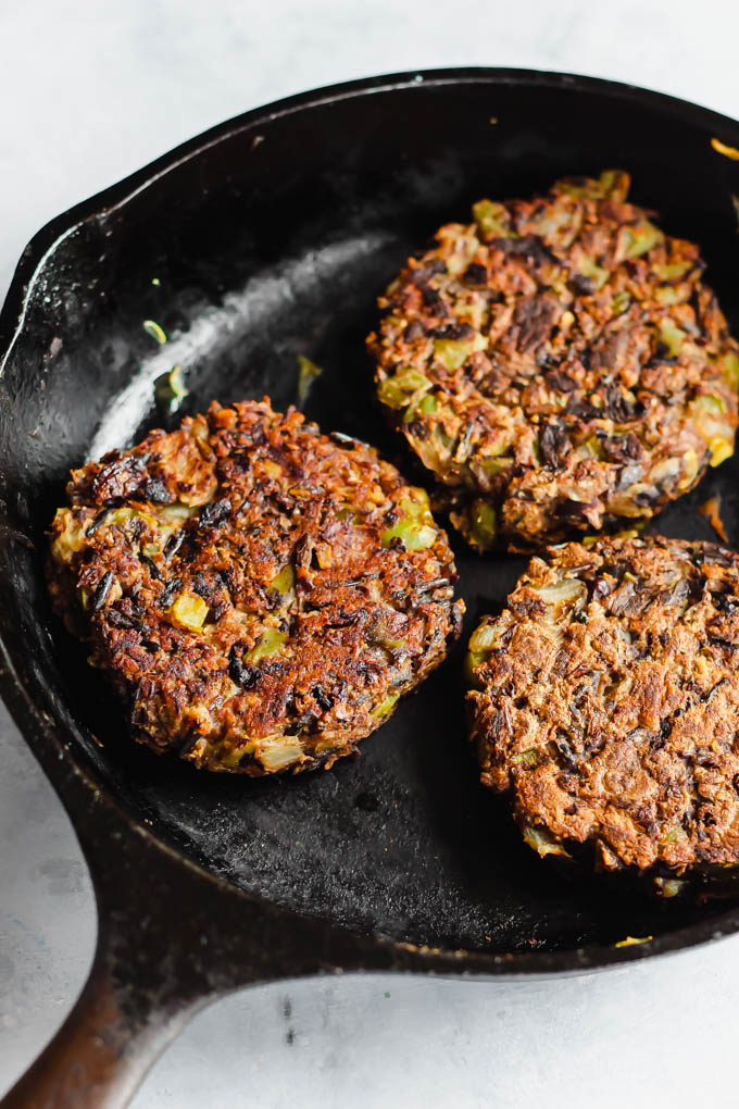 Three wild rice mushroom veggie burger patties cooking in a cast iron skillet