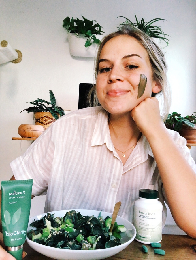 a woman wearing a face mask sitting in front of a bowl of greens