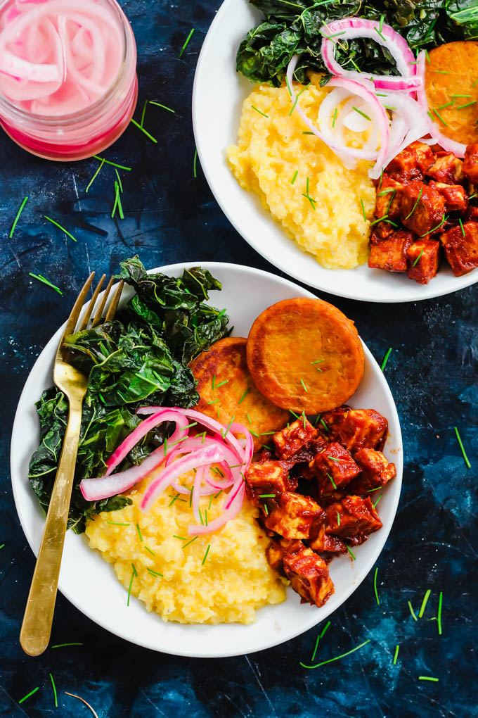 two bowls of vegan bbq tofu served with corn grits, collard greens and sweet potato hash browns