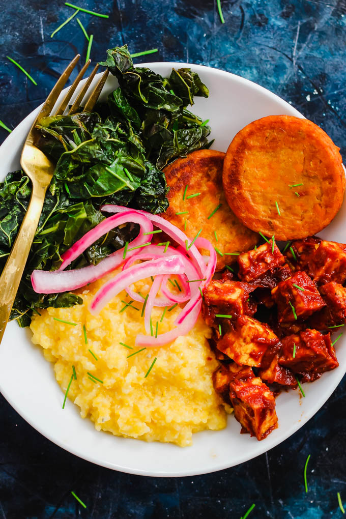 a bowl filled with vegan grits, collard greens, sweet potatoes, tofu and picked onions
