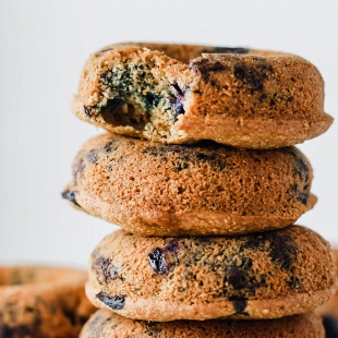 A stack of vegan blueberry doughnuts with a bite taken out of the doughnut on the top of the stack