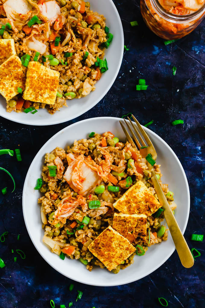 An overhead shot of two bowls of korean kimchi fried rice topped with tofu and green onions