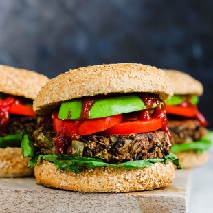 Three wild rice mushroom veggie burgers on a wooden cutting board topped with ketchup, avocado, lettuce and tomato