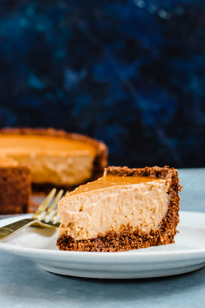 a single slice of vegan pumpkin cheesecake served on a plate in front of the full cheesecake