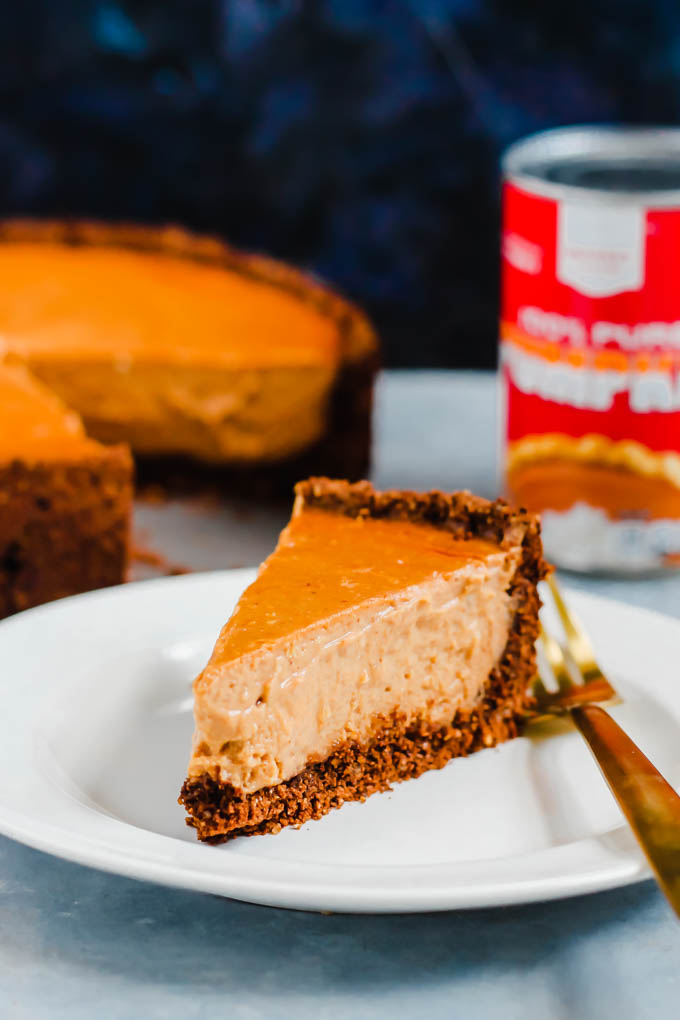 a slice of vegan pumpkin cheesecake with a full cheesecake in the background next to a can of pumpkin