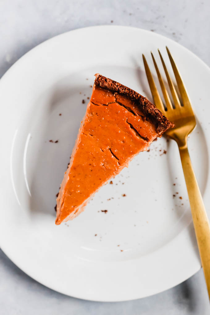 a slice of pumpkin cheesecake served on a white plate with a gold fork