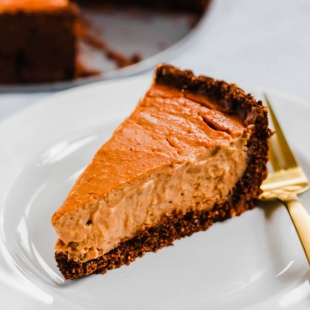 a slice of vegan pumpkin cheesecake served on a white plate with a gold fork